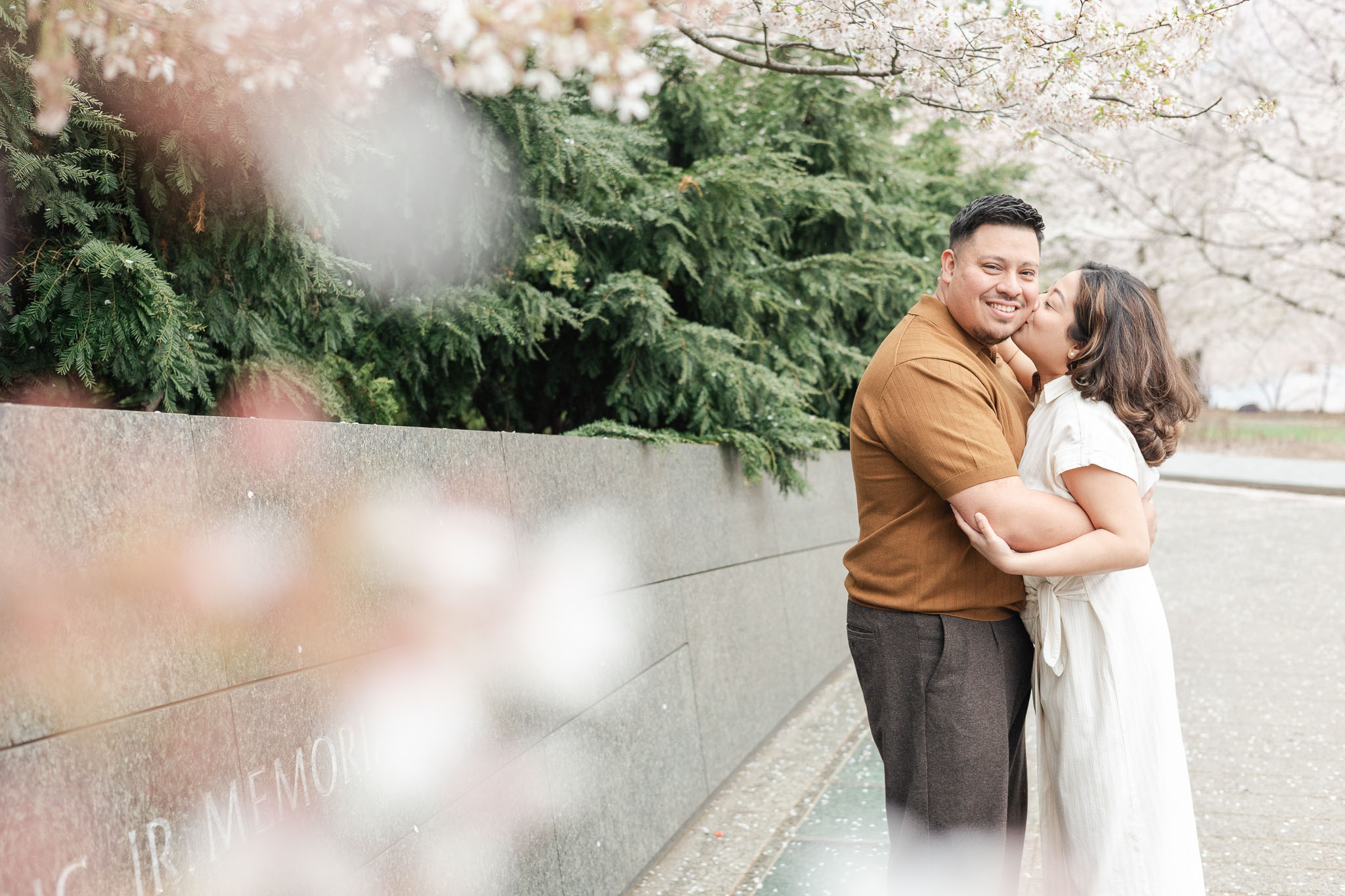 girl kissing guy's cheek amidst cherry blossoms