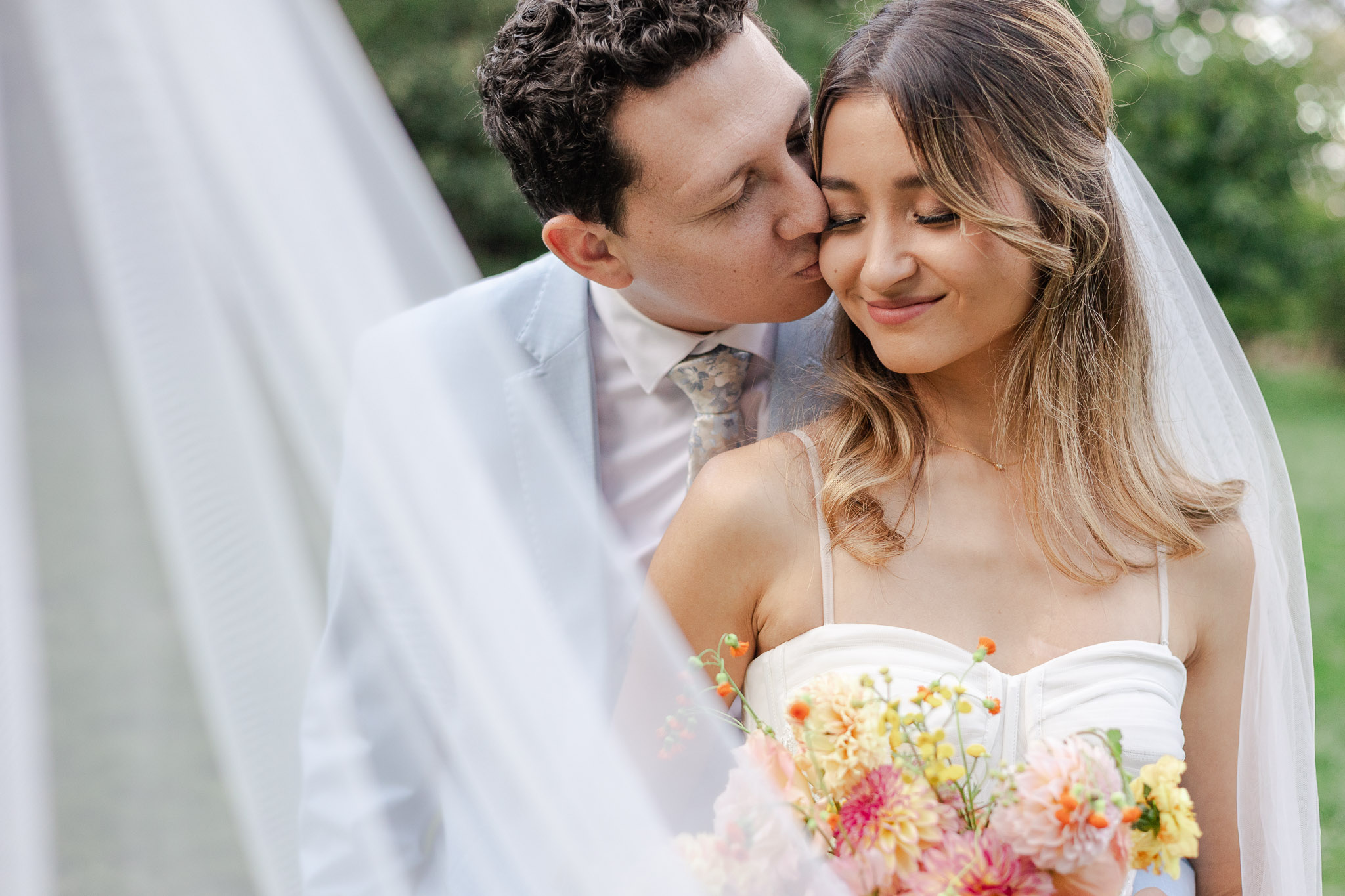 groom kissing bride on the cheek and veil sweeps across them